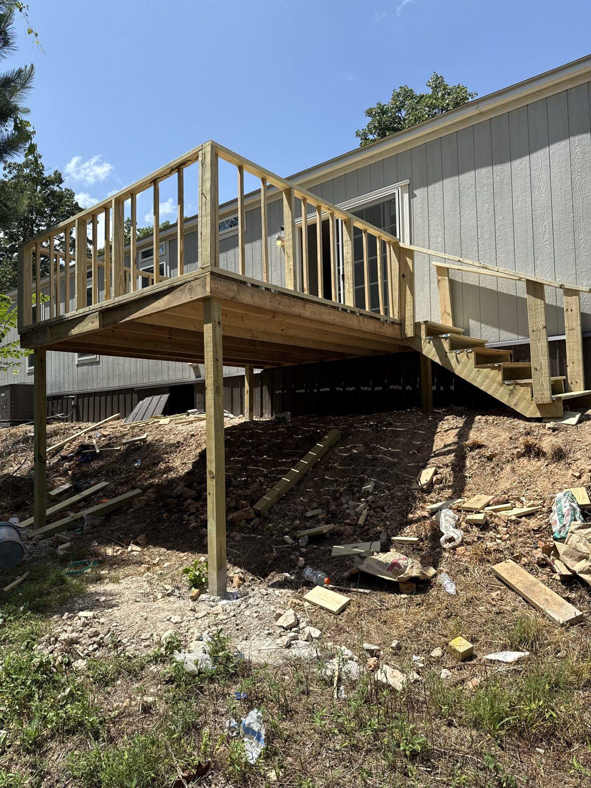New elevated deck with stairs and railing built onto a home on a sloped rural Oklahoma lot